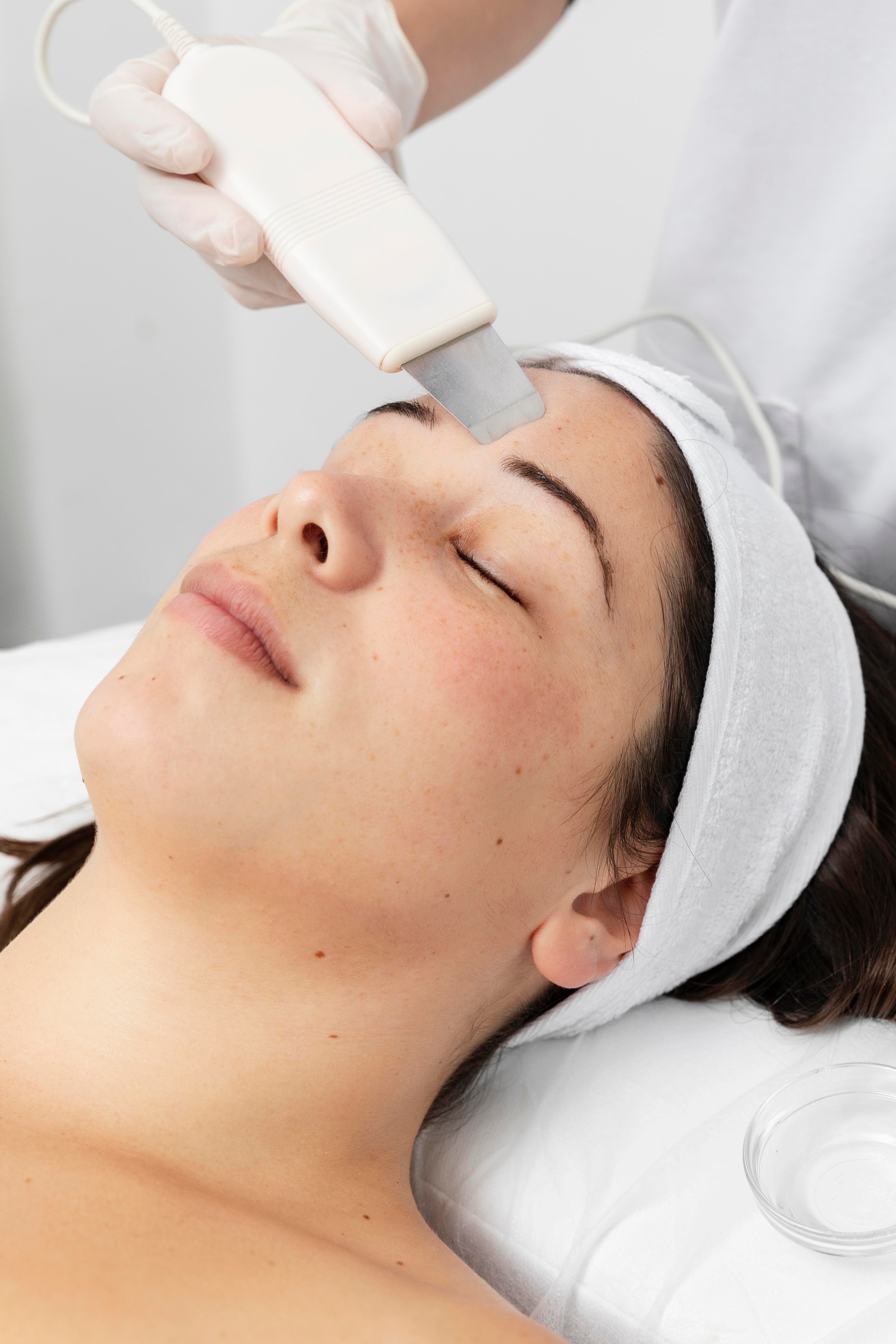 Mujer recibiendo tratamiento facial HIFU de Iderma. Profesional aplicando dispositivo en la frente de la paciente relajada